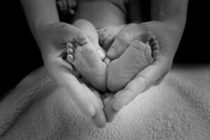 A pair of hands holding a pair of baby feet, and forming a heart shape.